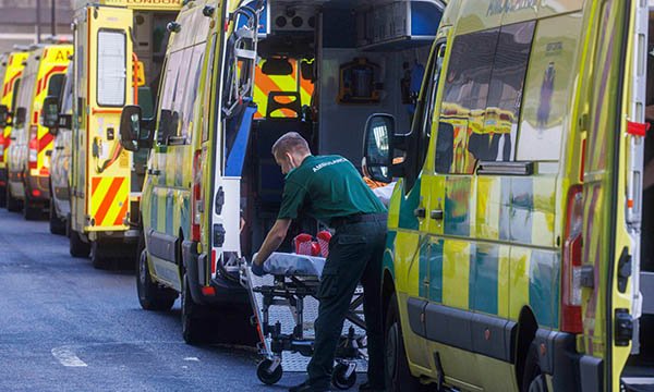 Multiple ambulances form a queue as one paramedic prepares a patient trolley