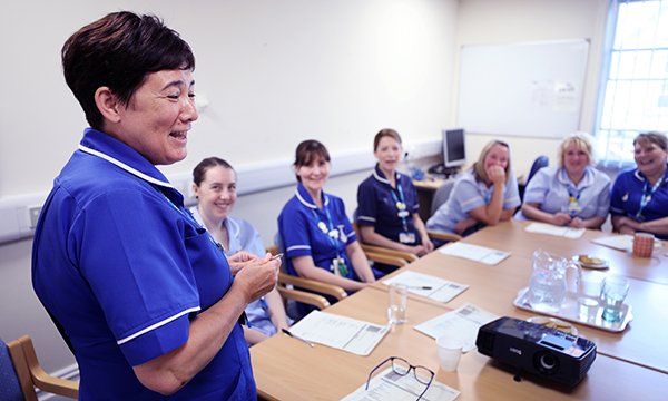 Photo of a nurse standing talking to other nurses who are sitting around a table