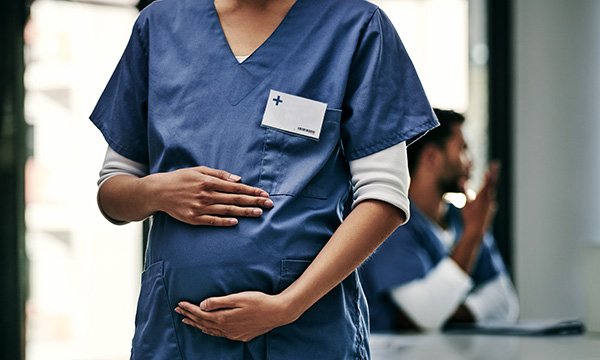Pregnant nurse wearing scrubs holds her bump – IFS study found pregnant nurses take shorter maternity leave if they work in teams where there are relatively more male nurses