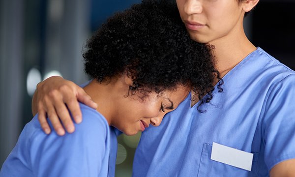 A nurse puts her arm around an upset colleague and comforts her