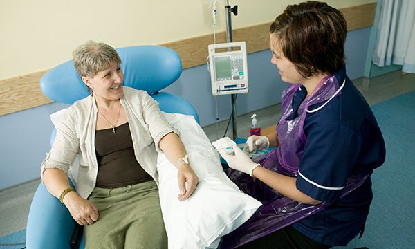 A nurse talking to a patient who is sitting down with their arm on a pillow and attached to a monitor
