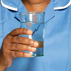 Close up image of a nurse in uniform holding a glass of water – one of the tips for nursing while coping with perimenopause symptoms is to stay hydrated