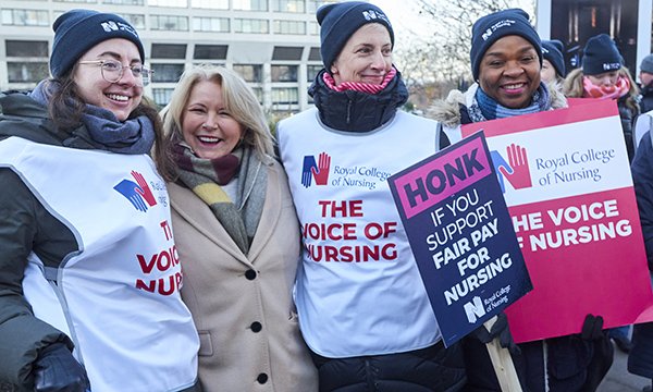 Photo of RCN general secretary Pat Cullen smiling and standing with three striking nurses on a picket line 