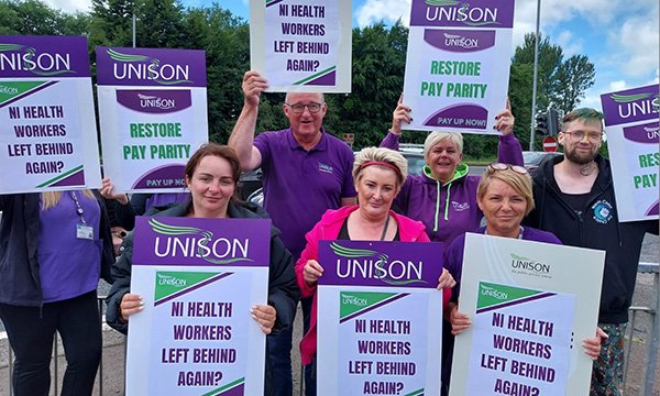 Members of Unison protest outside the Northern Ireland Office in Belfast holding placards that say 'NI health workers left behind again?'
