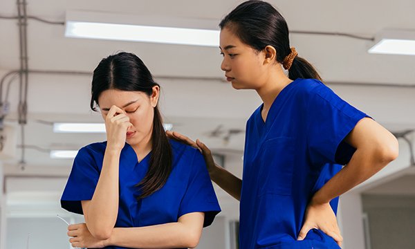 A nurse holds a hand to her face and appears upset, while another nurse touches her shoulder in sympathy 