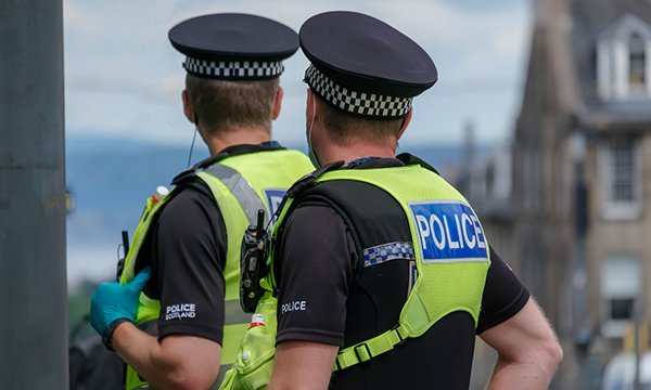Two officers in Police Scotland uniforms in the street, both looking at an incident away from the camera