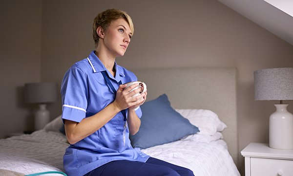 A nurse sits on a bed and looks anxious and full of self-doubt, as is common in imposter syndrome