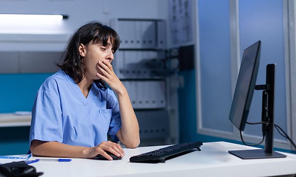 Photo of nurse yawning at work, illustrating story about NHS staff burnout