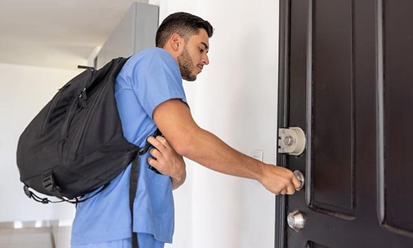 A nurse with a shoulder bag inserting a key into the door of an apartment 