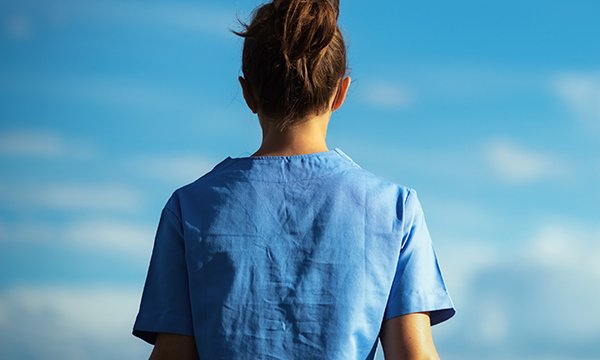 A nurse, seen from behind, looks up into a clear blue sky in an image representing an individual struggling with mental health issues