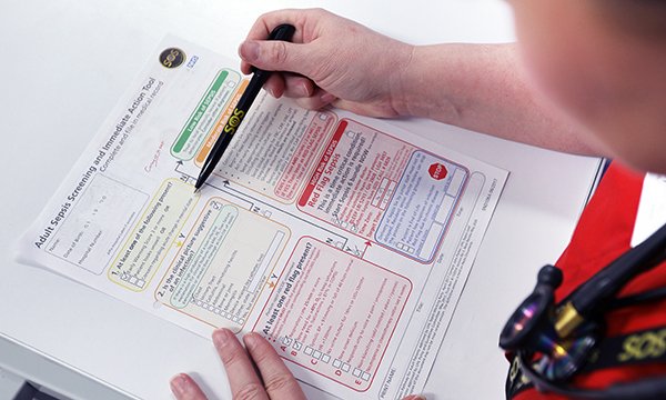 A medic places a pen next to a section of a document explaining adult sepsis screeningning