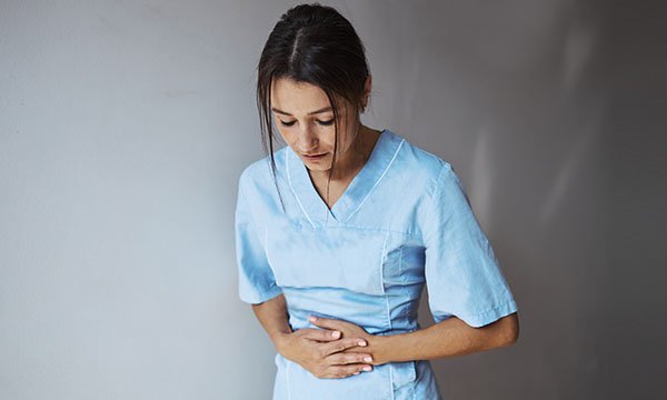 A nurse in a blue uniform clutches her stomach as though in pain
