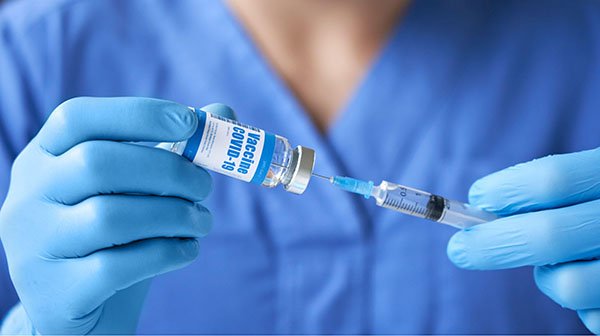 Nurse wearing gloves holding syringe and taking COVID-19 vaccine from vial