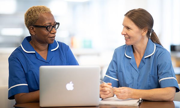 Two nurses in uniform sitting at a table with a laptop in front of them. E-posters, messaging and videos were fundamental to the Be PPE Free campaign