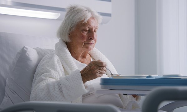An older woman sitting up in a hospital bed and eating a meal