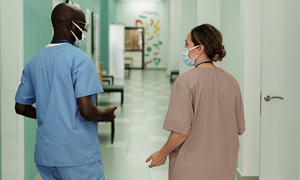 A nurse and a nursing associate chat in a hospital corridor