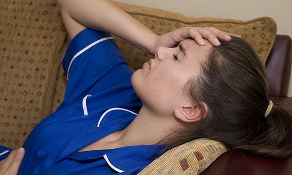 A nurse appears stressed as she leans back on a sofa with her eyes closed 