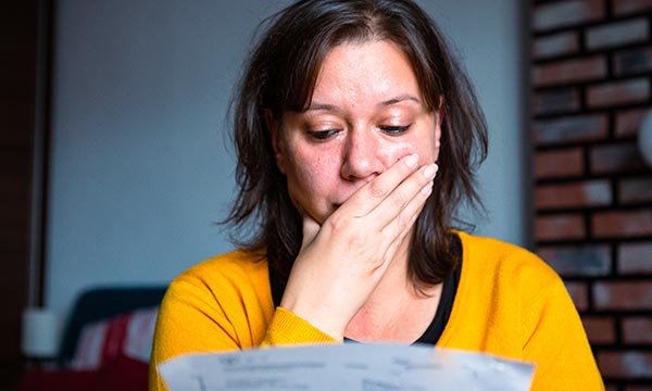 Woman looks distressed, with hand over her face, as she looks at official paperwork. Nurses say they are struggling with bills and cost of living