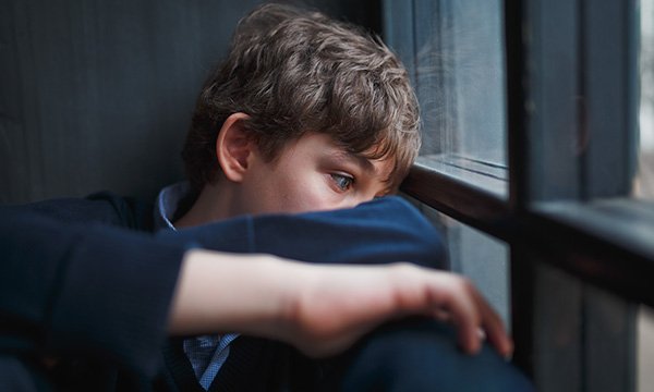 Picture shows a sad looking teenage boy sitting next to a window  