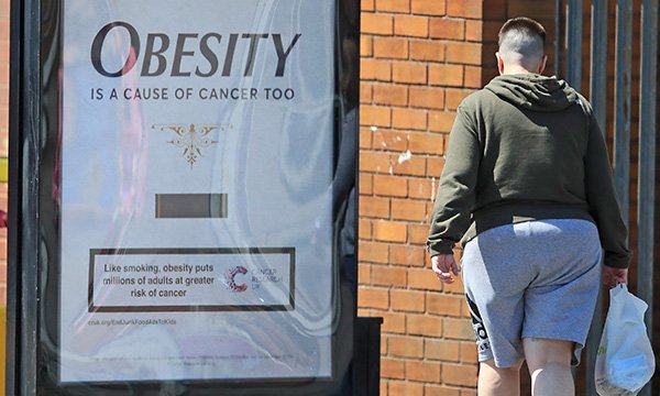 Someone looking at an besity causes cancer campaign poster