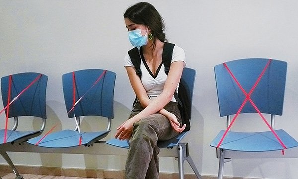A young woman waits to be seen by nursing staff in a near-empty hospital emergency department during the first wave of the COVID-19 pandemic