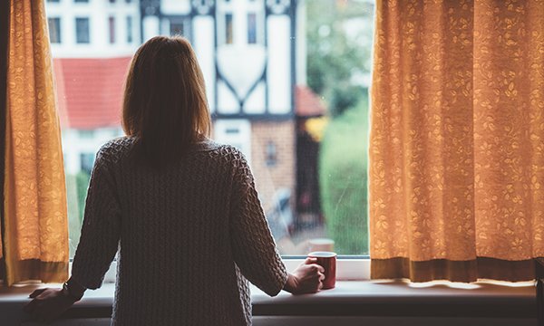 A woman standing alone at a window, looking outside. People who have had close, sustained contact with a person confirmed to have coronavirus are being told to self-isolate for 14 days