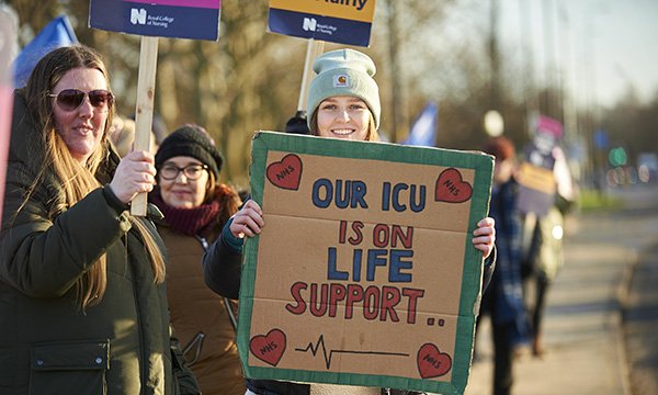 A woman on a picket line holds a placard saying Our ICU is on life support