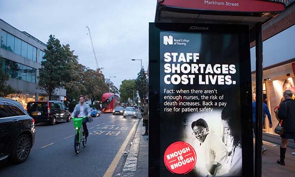 Photo of a poster on a bus shelter saying Staff Shortages Cost Lives