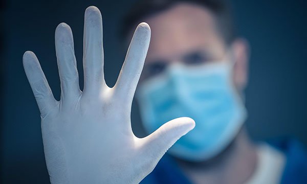 Picture of a medic wearing a mask and holding up his hand, wearing a glove, in a 'stop' gesture.