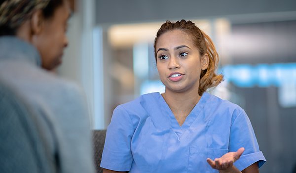 Picture shows a young woman in scrubs talking to a patient. Stress from the coronavirus and helping patients to cope with an uncertain future is stretching the resilience of nurses.
