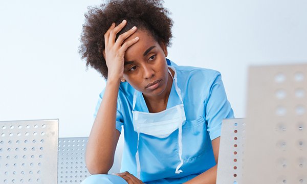 Picture shows a young nurse in scrubs looking weary with her hand to her head. Added stress from the coronavirus and helping patients to cope with an uncertain future is stretching the resilience of nurses.