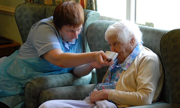 care home staff member helps resident drink