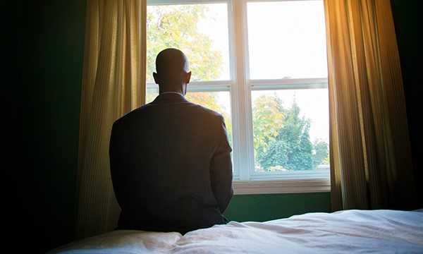 Silhouette of man sitting on bed, looking out window