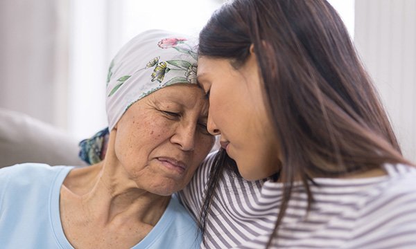 A patient with a terminal illness, who is wearing a headscarf, being comforted by another person