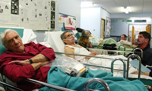 patients lying on trolleys in a busy waiting area shows pressures hospitals can face 