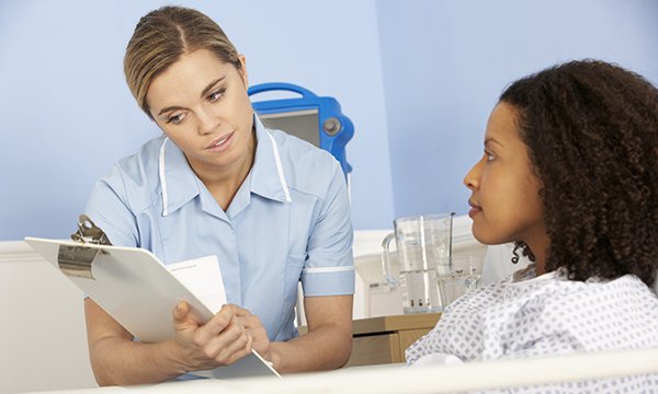 nurse sits by a patient's bedside looking at her clipboard 