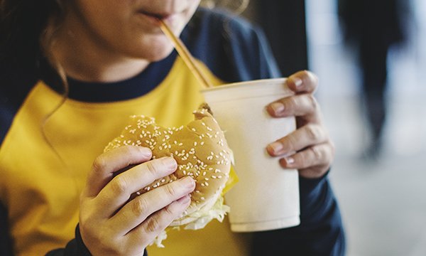 child eats holds burger while sipping a drink from a straw 