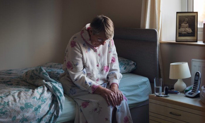 woman sits in her dressing gown on the edge of her bed