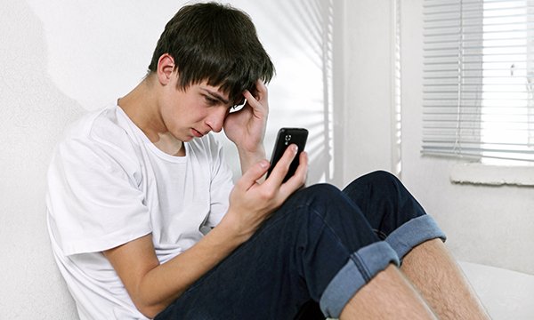 Picture shows a boy, seated, looking intently at a mobile phone. New guidance aims to improve recognition and management of depression in children aged five to 18 and promote effective treatments.
