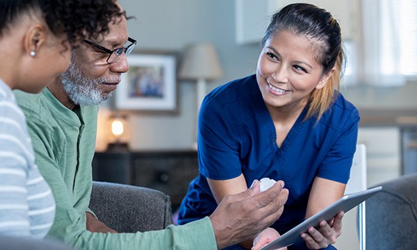 Picture shows a community nurse at the home of an older man and his daughter. In this article Ian Bailey says the technology exists for multidisciplinary teams to instantly share updated patient records, and nurses must be given access to it.
