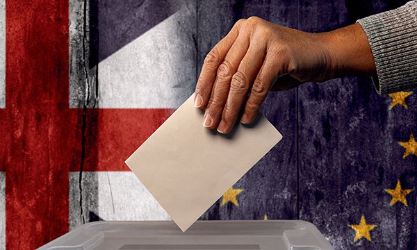 Stock image of a vote going in to a ballot box, with british and EU flags in the background