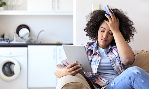 Picture shows perplexed young woman holding a credit card and tablet computer. An RCN report on why nurses have been historically underpaid calls for fairer and more realistic job evaluation frameworks.