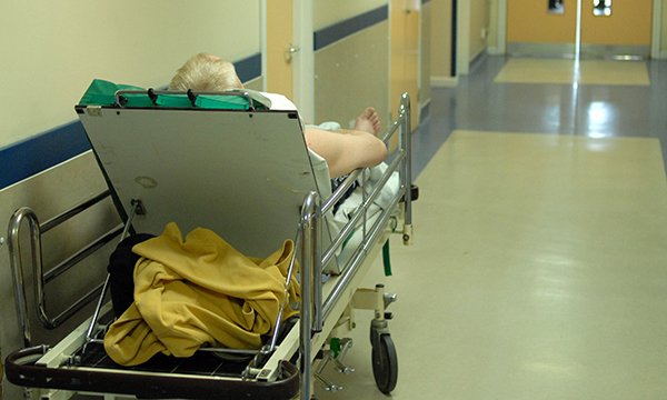 patient seen from behind, lying on a trolley in a hospital corridor
