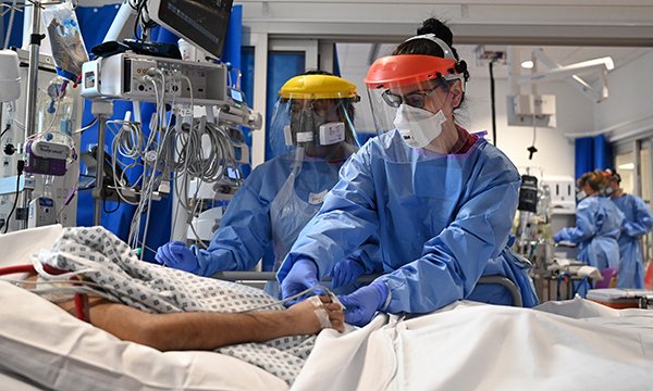 nurses wearing PPE at a patient's bedside in ICU