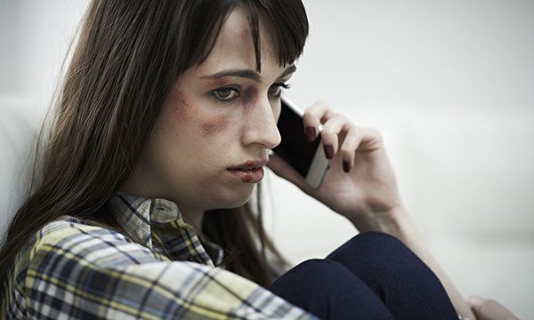 woman with bruised face looks sad as she makes a phone call