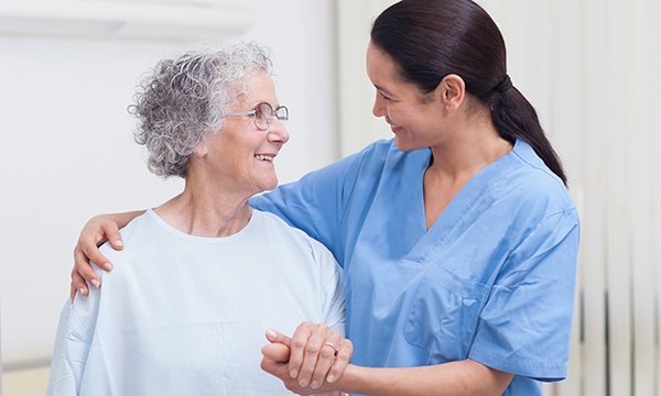 nurse puts supportive shoulder around woman's shoulders and both smile at each other