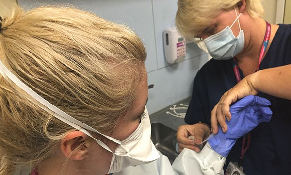 Picture shows a nurse being helped to put on personal protective equipment
