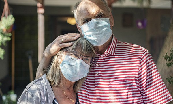 Picture shows an older couple wearing masks and looking solemn