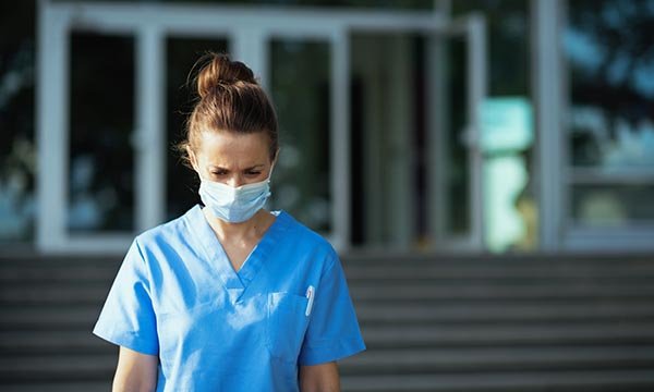 A nurse stands outside a building looking despondent