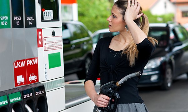 A woman at a petrol station appears worried as she looks at the price gauge